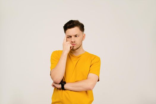 Lost in thought or deep in thought handsome young man folded his hands and holding his face with his hand. Young casual man in yellow t-shirt portrait isolated on white background.