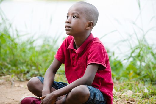 portrait of little boy sitting cross-legged alone in nature at the edge of a lake