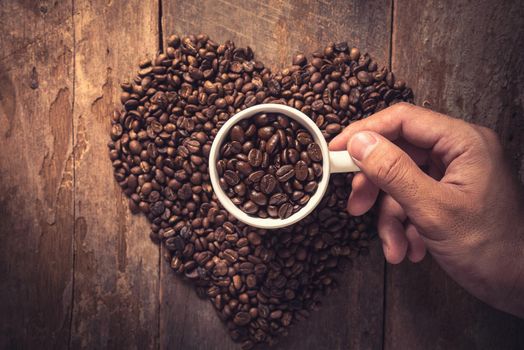 Man hand holding coffee cup and coffee bean on wooden table, Vintage color