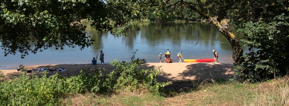 saumur, france, 12 august 2021: family drags canoes to river loire on warm summer day in french Parc naturel regional Loire-Anjou-Touraine