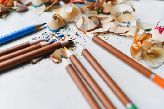 Wooden colorful pencils with sharpening shavings, on a white table
