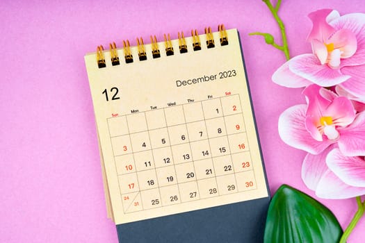 December 2023 calendar desk and pink orchid on pink background.