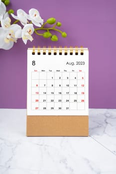 August 2023 calendar desk and white orchid on purple background.