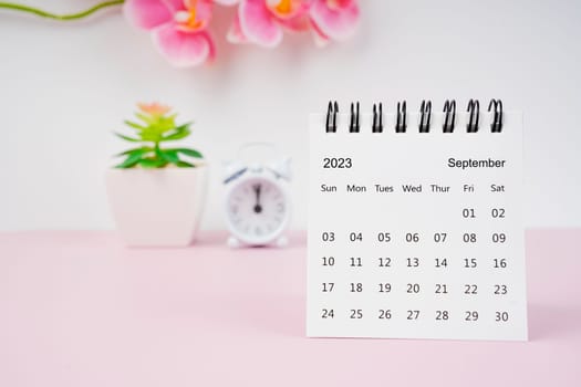 September 2023 desk calendar and pink orchid with alarm clock.