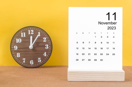November 2023 Monthly calendar for 2023 year with clock on yellow table.