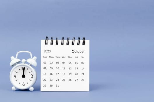 October 2023 desk calendar and alarm clock on blue color background.