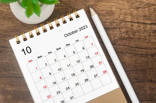 October 2023 desk calendar for 2023 with pencil on wooden background.