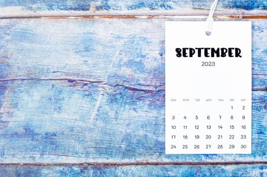 September 2023 calendar page hanged with white rope on old blue wooden background.