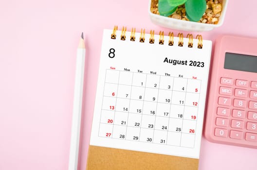 August 2023 desk calendar for 2023 year with calculator on pink color background.
