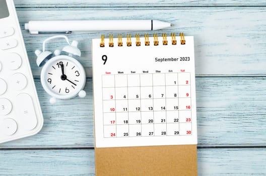 September 2023 Monthly desk calendar for the organizer to plan 2023 year with alarm clock and calculator on wooden table.