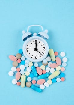 Medicine time. High angle view of colorful medicines and pills on alarm clock on the blue background.