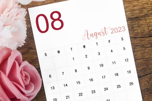 August 2023 Monthly calendar for 2023 year with pink rose on wooden background.