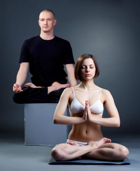 Meditating yoga trainers posing in studio, on gray background