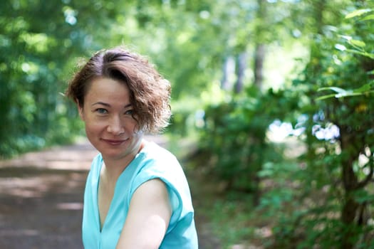 Portrait of a young smiling woman dressed in a blue T-shirt posing for the camera in a park.