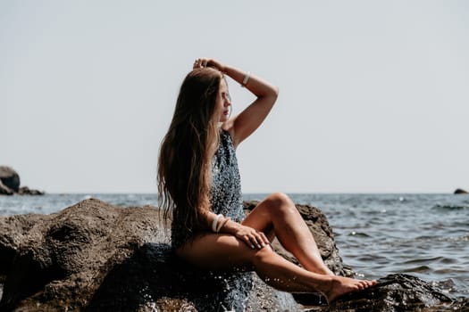 Woman travel sea. Young Happy woman in a long red dress posing on a beach near the sea on background of volcanic rocks, like in Iceland, sharing travel adventure journey