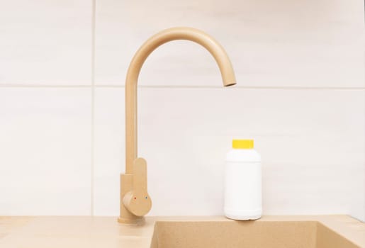 Pipe Drain Granules in White Plastic Bottle With Yellow Cap On Kitchen Sink In Cook Room. Clog Cleaner, Housework Help. Cleaning enzymes, Prevention of Blockages In Traps. Horizontal plane.