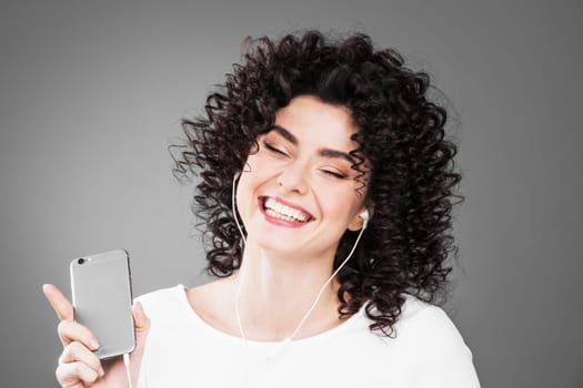 Woman in white dancing with earphones headphones listening to music on phone, gray background