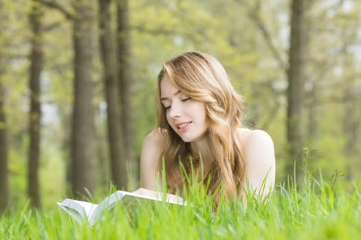 Young beautiful woman lays on green grass field and reads book, spring exam concept, copy space for text