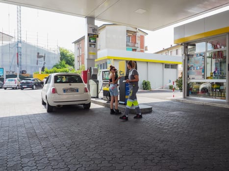 Cremona, Italy - July 3 2023 gas station attendant woman taking payments with credit card from customers outdoors near fuel pumps