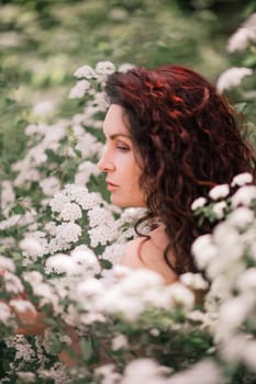 Woman spirea flowers. Portrait of a curly happy woman in a flowering bush with white spirea flowers