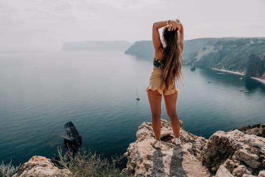 Woman travel sea. Happy tourist taking picture outdoors for memories. Woman traveler looks at the edge of the cliff on the sea bay of mountains, sharing travel adventure journey.