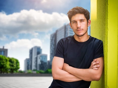 Head and shoulders shot of one handsome young man with green eyes in urban setting, looking at camera, wearing t-shirt