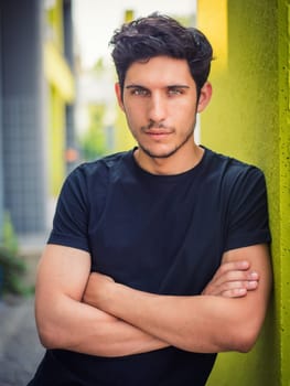 Head and shoulders shot of one handsome young man with green eyes, in urban setting leaning against a wall, looking at camera, wearing t-shirt