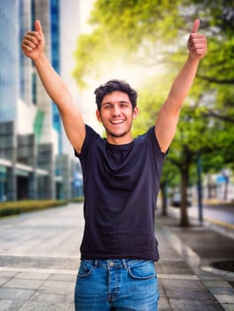 Head and shoulders shot of one handsome young man with green eyes laughing, in urban setting, looking at camera, wearing t-shirt