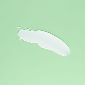 Smear of white cream for face and body on a green background