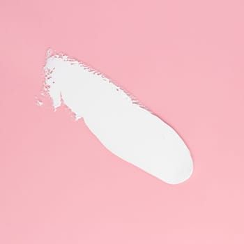 Smear of white cream for face and body on a pink background