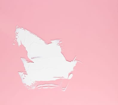 Smear of white cream for face and body on a pink background