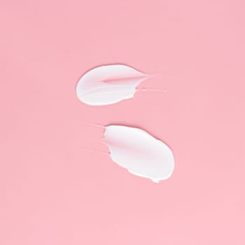 Smear of white cream for face and body on a pink background