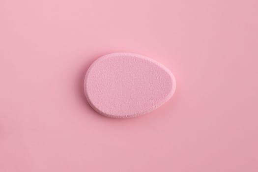 Cosmetic sponge in the shape of an egg on a pink background. Top view