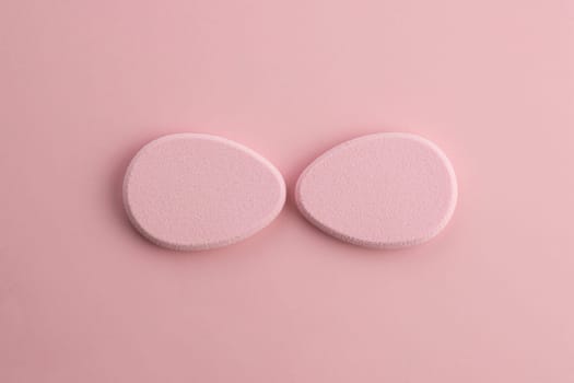 Cosmetic sponge in the shape of an egg on a pink background. Top view