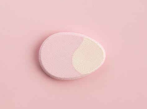 Cosmetic sponge in the shape of an egg on a pink background. Top view