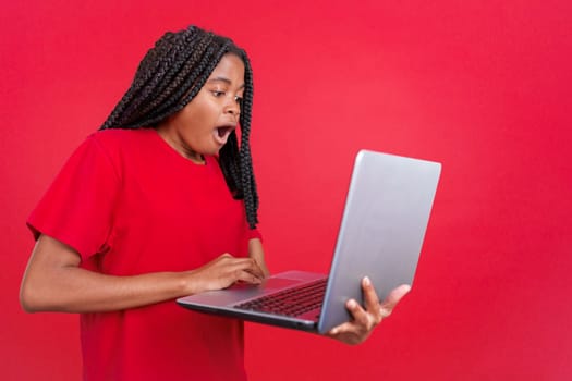 African woman with a surprised look using a laptop in studio with red background