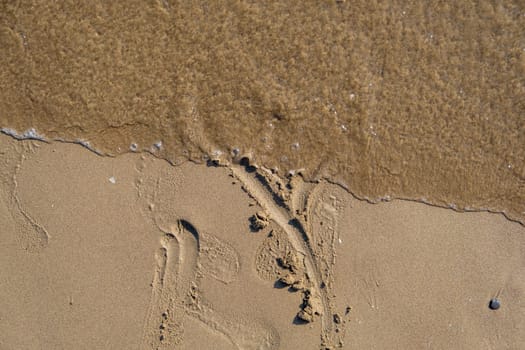 Drawing heart shape love concept on sand at the beach with vacation holiday summer travel background. Heart shape and footprint on wet sand.