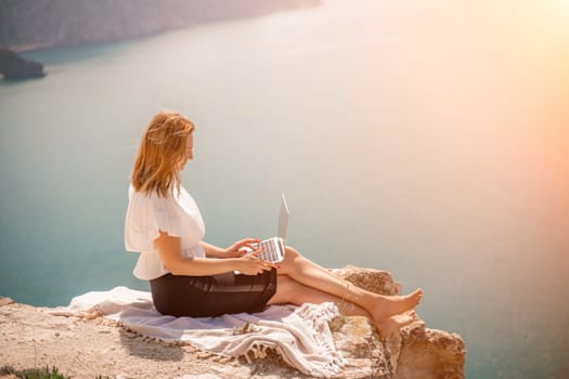 Freelance woman working on a laptop by the sea, typing away on the keyboard while enjoying the beautiful view, highlighting the idea of remote work