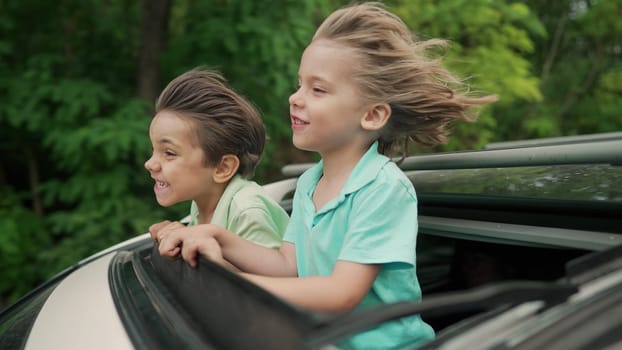 Adorable happy little kids stands in open car sunroof during road trip in countryside at summer. Concept of family leisure, active traveling. High quality