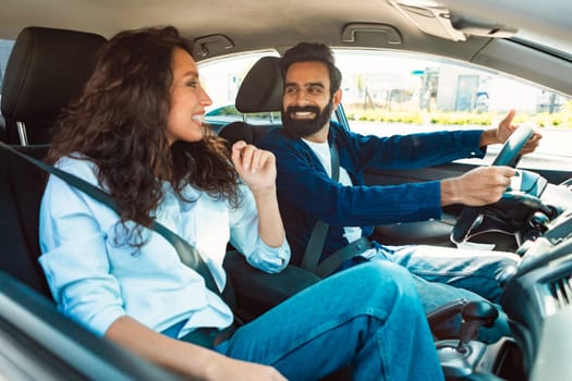 Test drive. Happy young middle eastern couple driving in new car and talking, discussing automobile while testing vehicle, man driver sitting behind the wheel