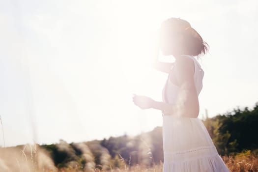 Spirit of freedom. An attractive boho girl in blouse, hat and sunglasses standing on the field on the background of a blue sky. Summer vacation, traveling. Bohemian, modern hippie style