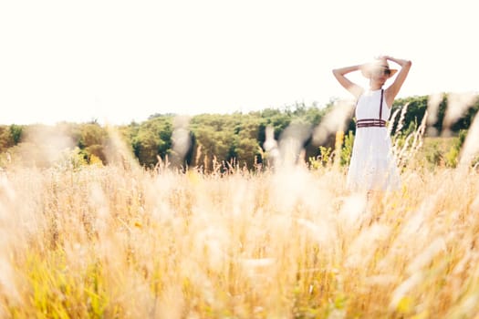 Spirit of freedom. An attractive boho girl in blouse, hat and sunglasses standing on the field on the background of a blue sky. Summer vacation, traveling. Bohemian, modern hippie style