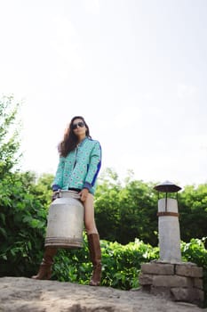 Young fashionable farmer woman posing on camera while holding milk can.