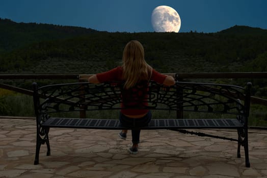 Blonde girl sitting on a bench with her back facing the moon.unrecognisable, caucasian, straight hair, red, forest, lonely, forge, maderam pines, relaxation , contemplation