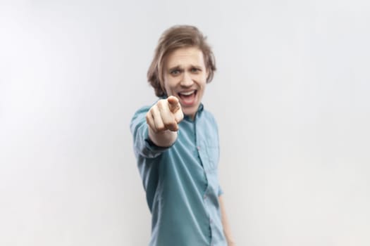 Portrait of overjoyed cheerful joyful young man standing pointing at camera, selecting you, smiling, expressing positive emotions, wearing blue shirt. Indoor studio shot isolated on gray background.