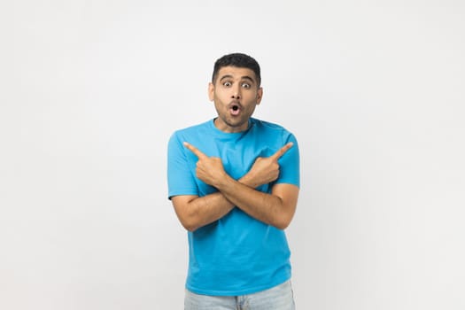 Portrait of shocked surprised astonished young adult unshaven man wearing blue T- shirt standing pointing with index fingers to different size. Indoor studio shot isolated on gray background.