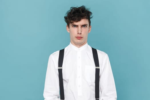 Portrait of surprised astonished shocked man wearing white shirt and suspender looking at camera with puzzled confused expression. Indoor studio shot isolated on blue background.