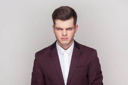 Portrait of sad upset depressed handsome man standing looking at camera with sorrow and sadness, being offended, wearing violet suit and white shirt. Indoor studio shot isolated on grey background.