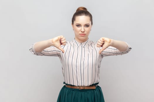 Portrait of dissatisfied displeased attractive woman wearing striped shirt and green skirt standing showing dislike gesture, looks unhappy. Indoor studio shot isolated on gray background.