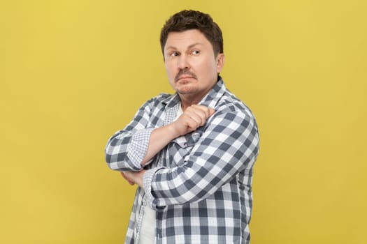Portrait of pensive handsome middle aged man in casual checkered shirt standing with thoughtful facial expression, looking away, thinking. Indoor studio shot isolated on yellow background.